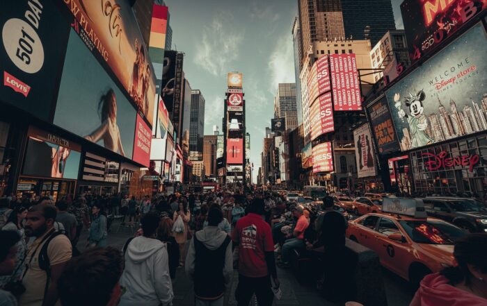 A crowded city street with people walking and standing in front of billboards.