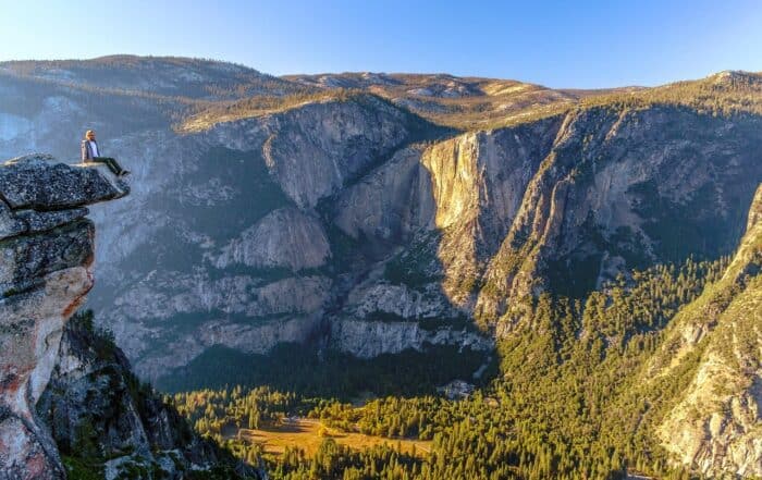 A man is sitting on the edge of a cliff overlooking a valley.