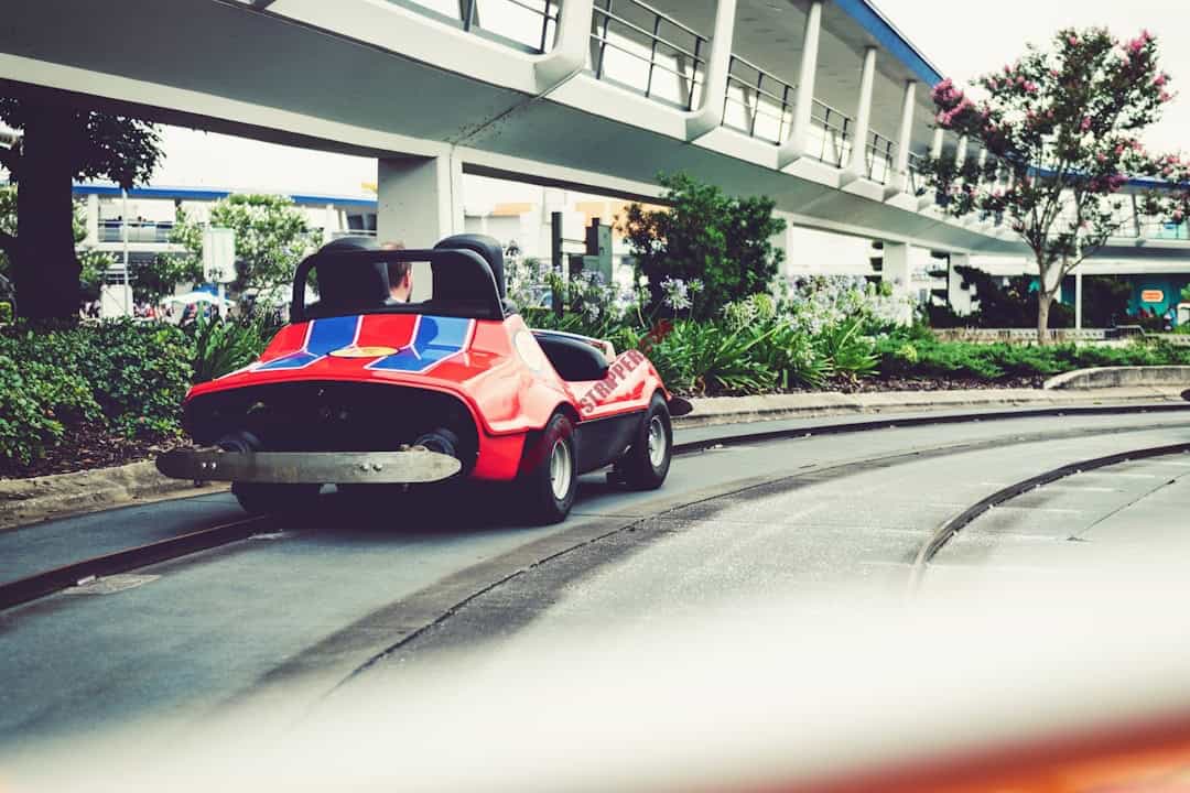 A red car driving down a track in front of a building.