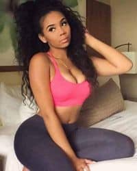 A woman in pink top and black leggings sitting on a bed.