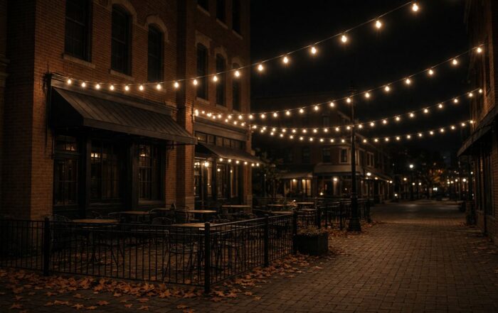 An empty Kansas City brick street at night with string lights and autumn leaves.